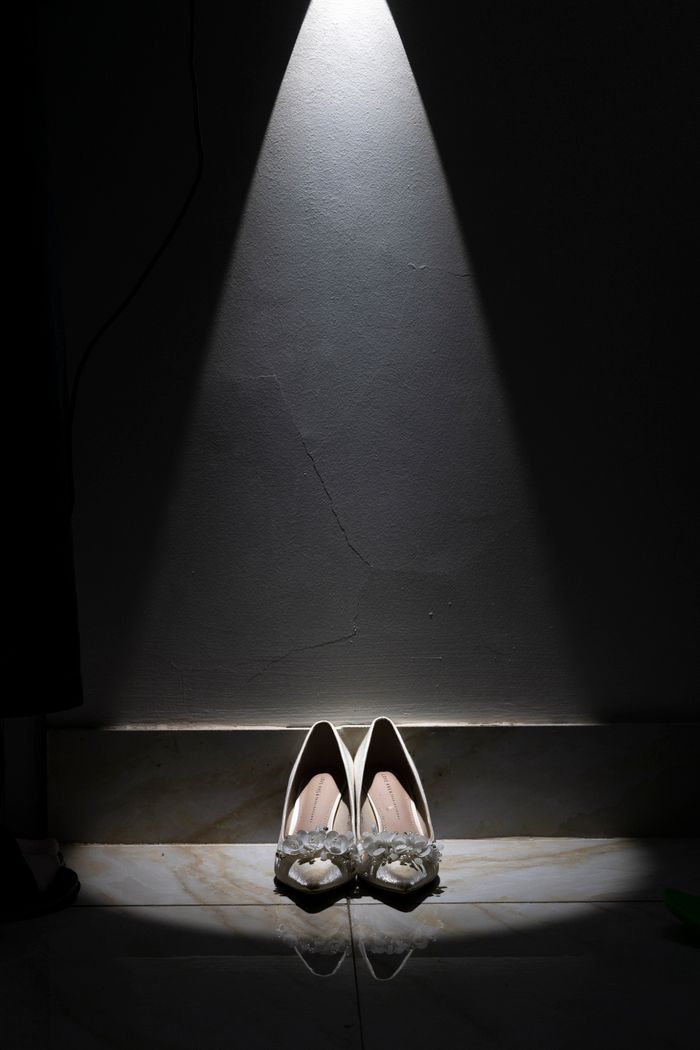Pair of white high heels illuminated by a spotlight against a dark background.