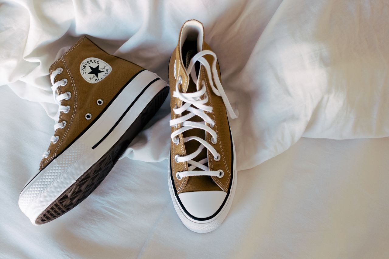 Brown Converse sneakers with white laces resting on white bed linen.